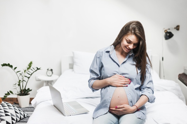 kobieta w ciąży siedzi na łóżku z laptopem