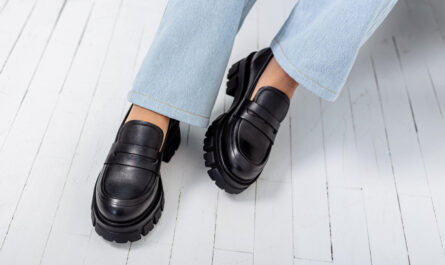 mloda kobieta o smuklych pieknych nogach w modnych czarnych skorzanych butach siedzi na krzesle w studio zblizenie na stylowe mokasyny damskie wiosenna kolekcja butow